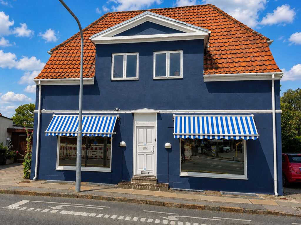 Front facade of Blue House with blue exterior, red tiled roof and striped awnings