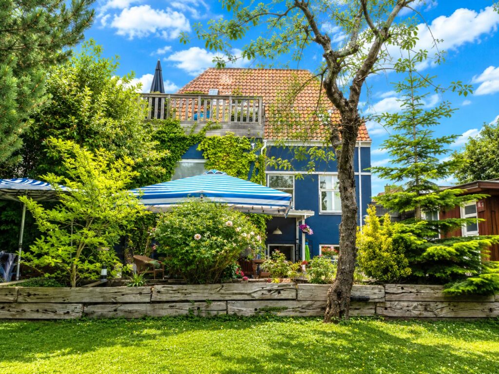 Rear view of the Blue House overlooking the private garden with terraces, mature landscaping, apple trees and plum trees.