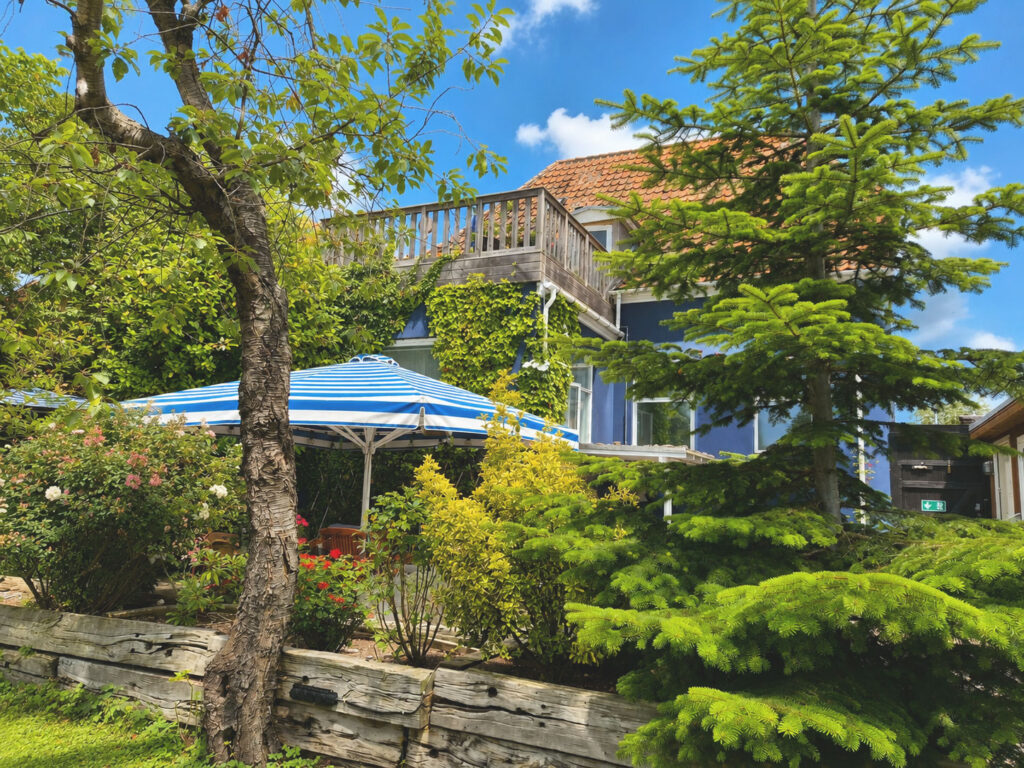 View of the Blue House featuring a spacious ground-floor terrace with a professional parasol, integrated lighting and heating, plus a private first-floor roof terrace overlooking the secluded landscaped garden with mature apple and plum trees.